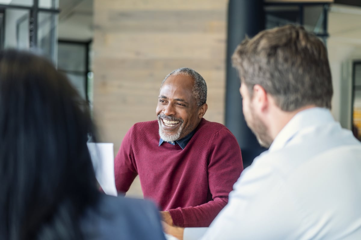 Smiling mature male manager sitting with colleagues in board room. Multi-ethnic professionals are planning strategy during meeting. They are at new office.