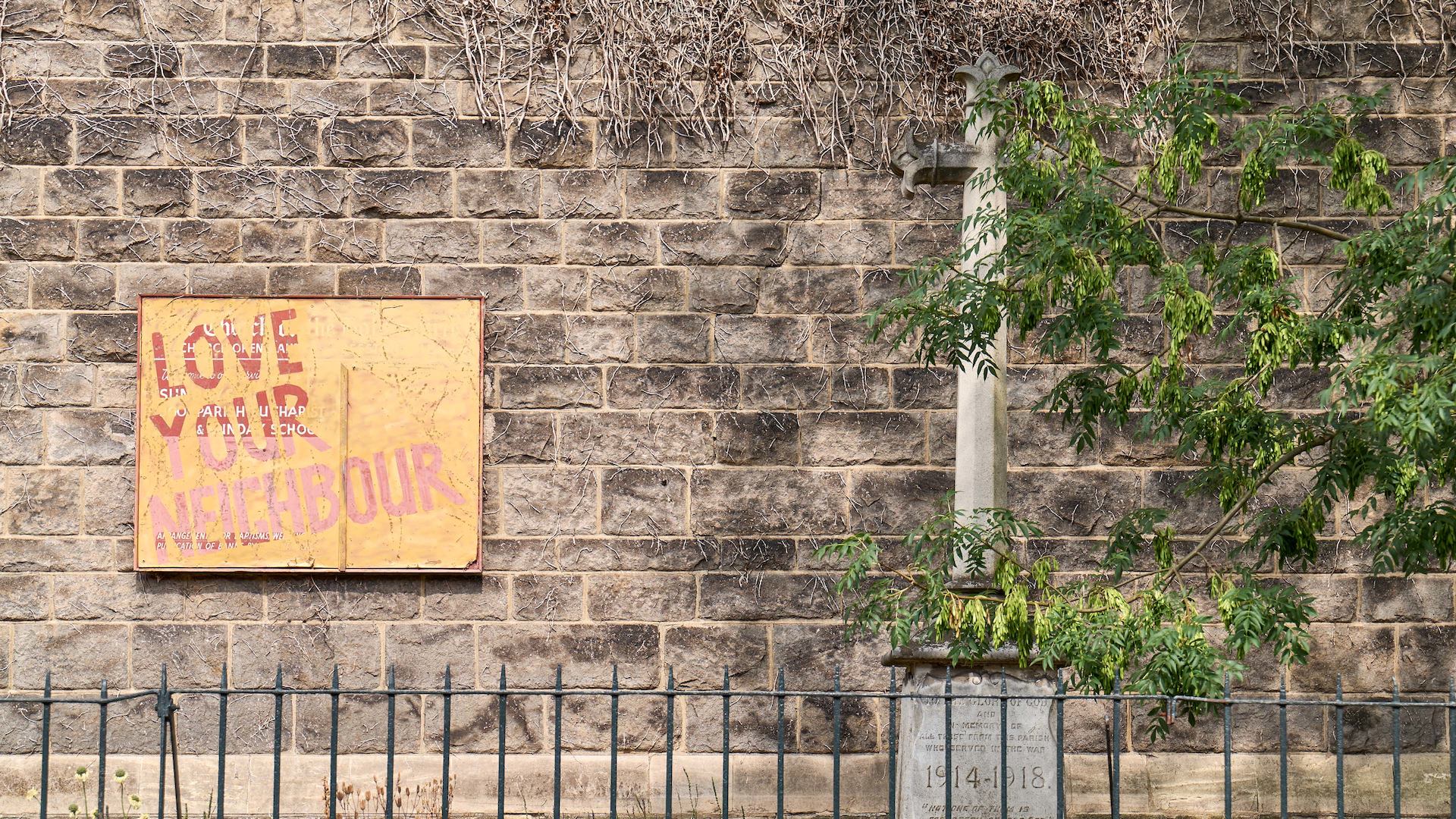 Brick wall with 'love your neighbour' sign.