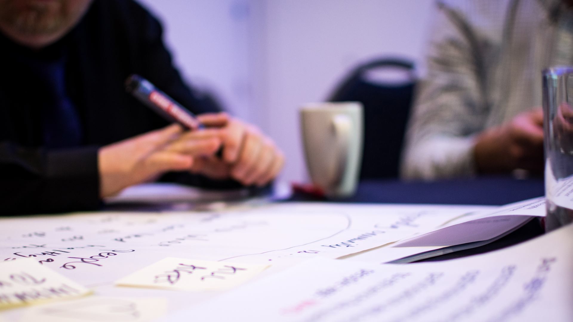 Person's hand with pencil and brainstorming sheets laid out on table with coffee mug.