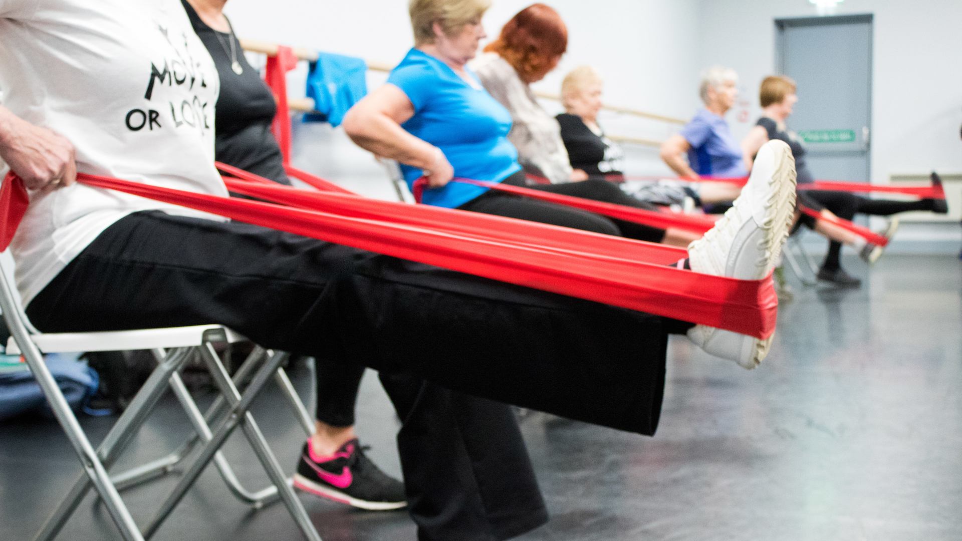 Women seated in exercise class using stretch bands on their legs.