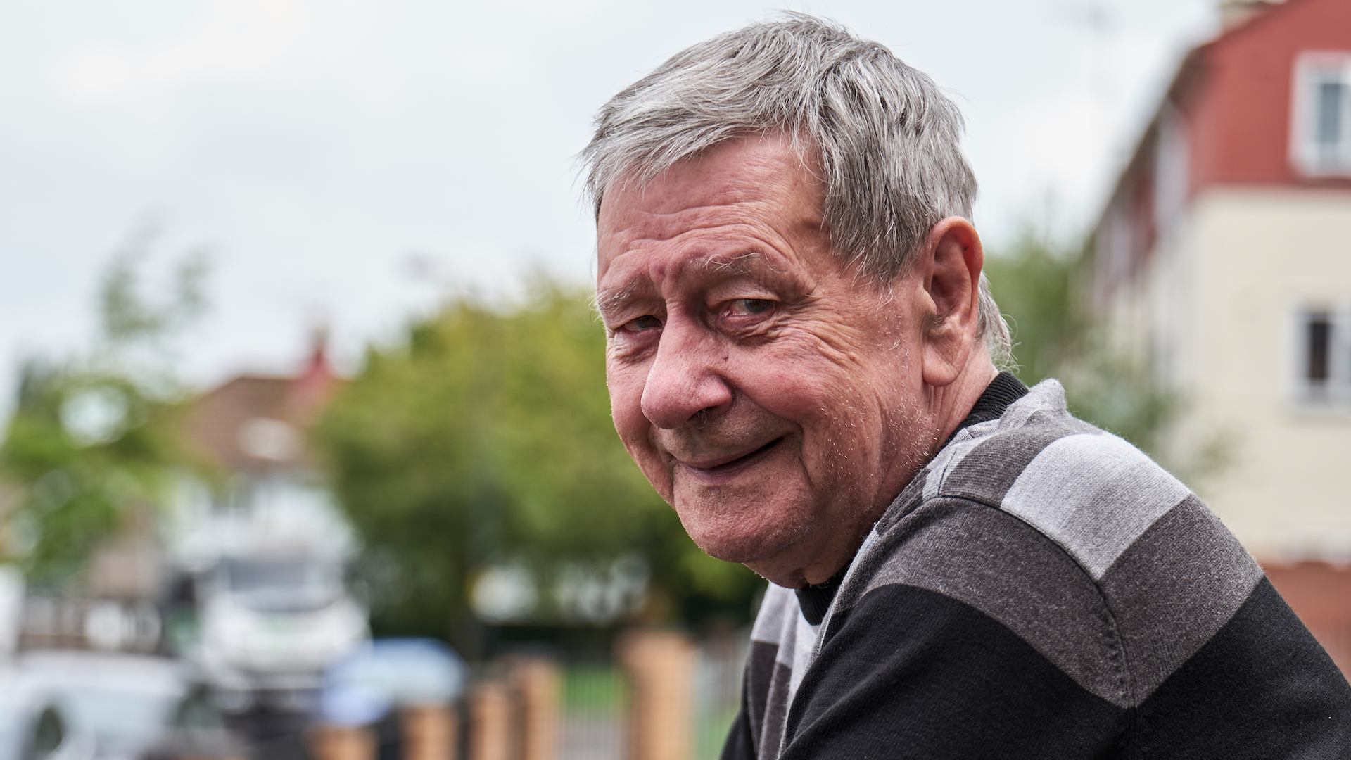 Older man looking into camera, leaning on fence