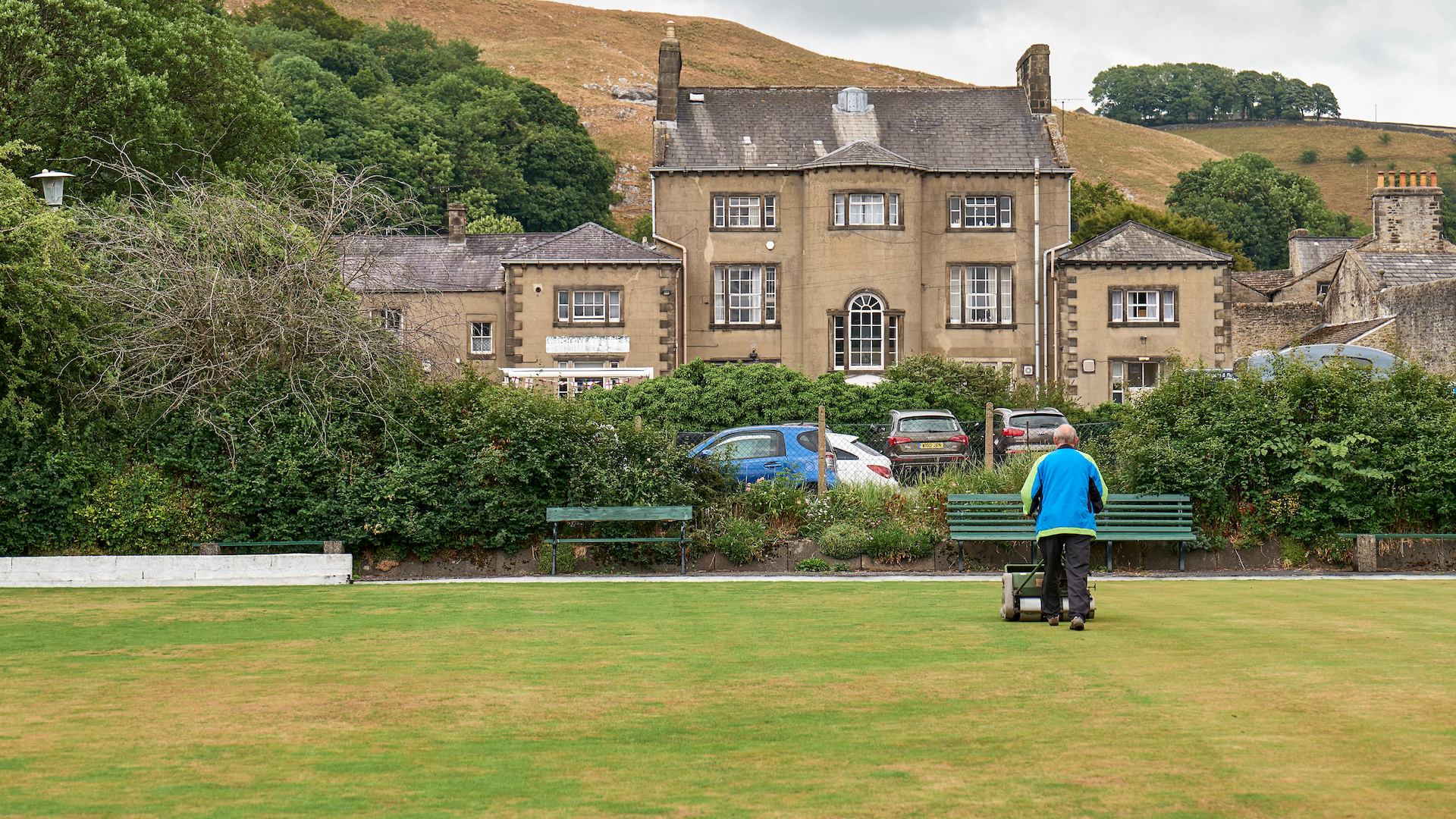 Landscape of hill and older man mowing grass
