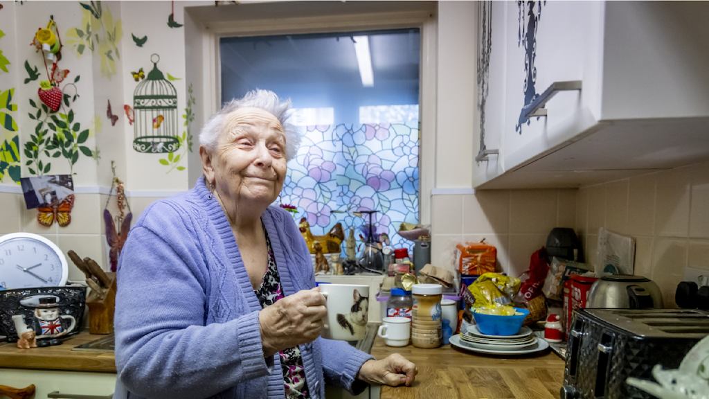 An older woman in her kitchen with a mug of tea