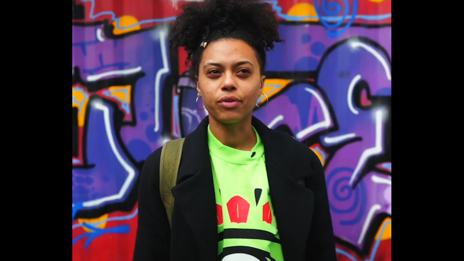 Thumbnail of video, showing younger woman standing by graffiti