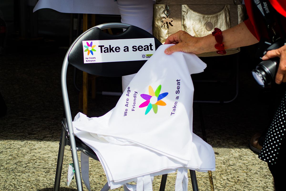 Folded chair with Take a seat campaign label and Take a seat campaign tote bags.