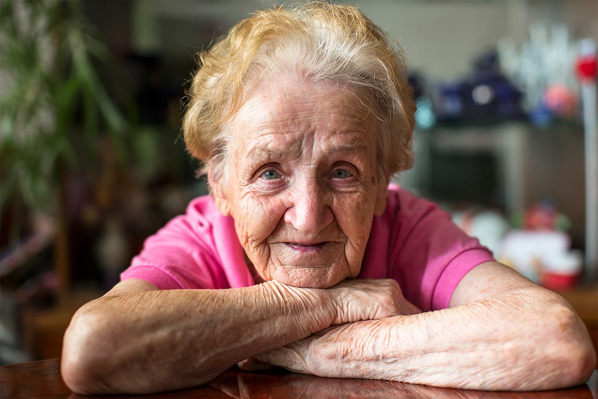 Elderly woman in pink t-shirt resting her chin on crossed arms.